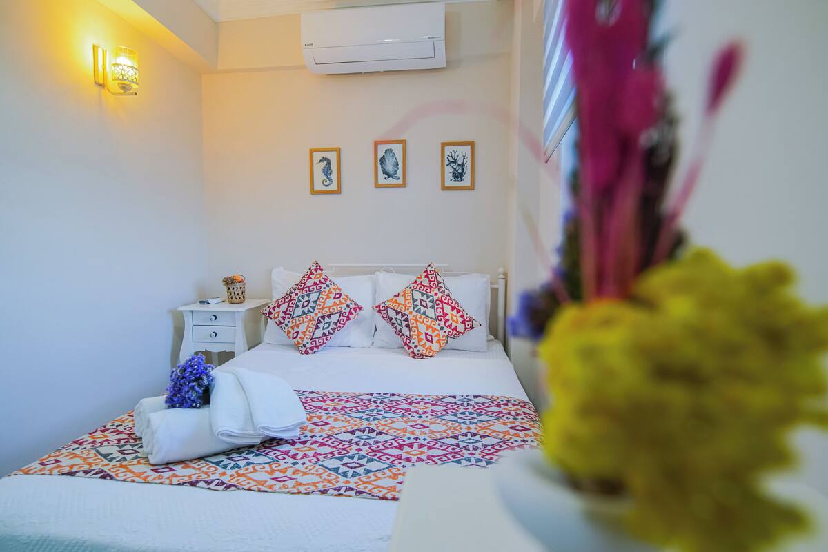 A neatly made bed with patterned pillows, a bedside table with a lamp, and wall-mounted artwork.