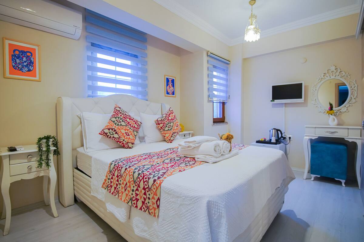 A neatly arranged bedroom with a bed, bedside tables, a TV, and a mirror.