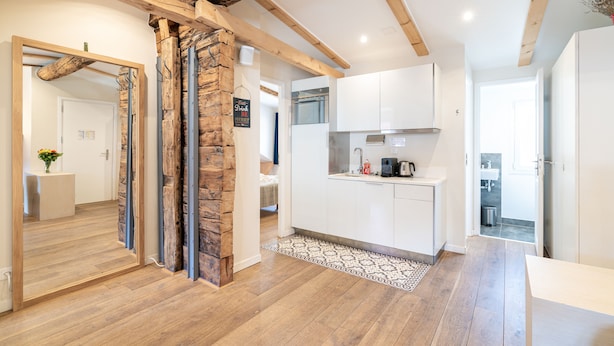 A modern kitchen with white cabinets, a wooden ceiling, and a patterned rug.