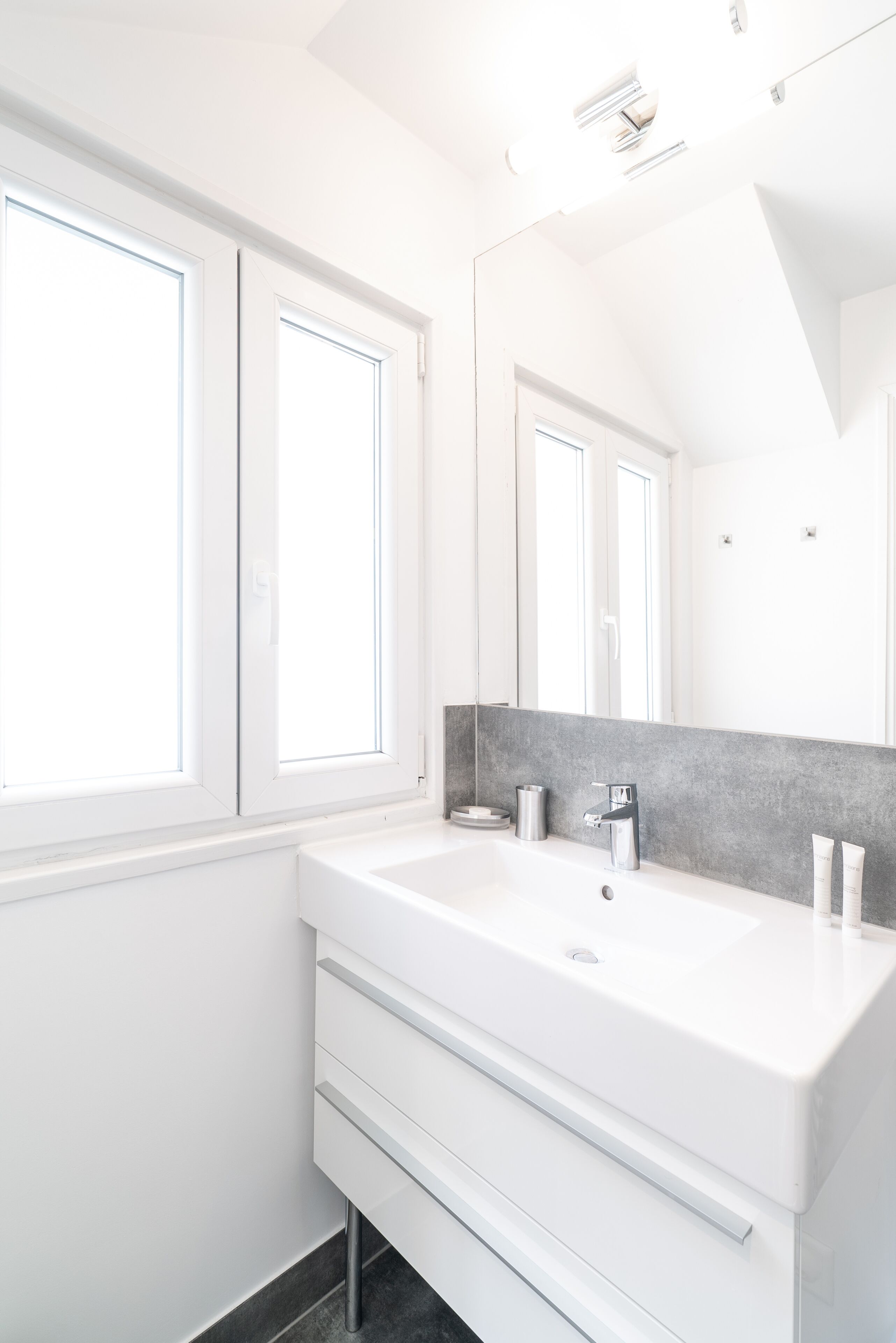 A modern bathroom with a large white sink, a mirror, and a window.