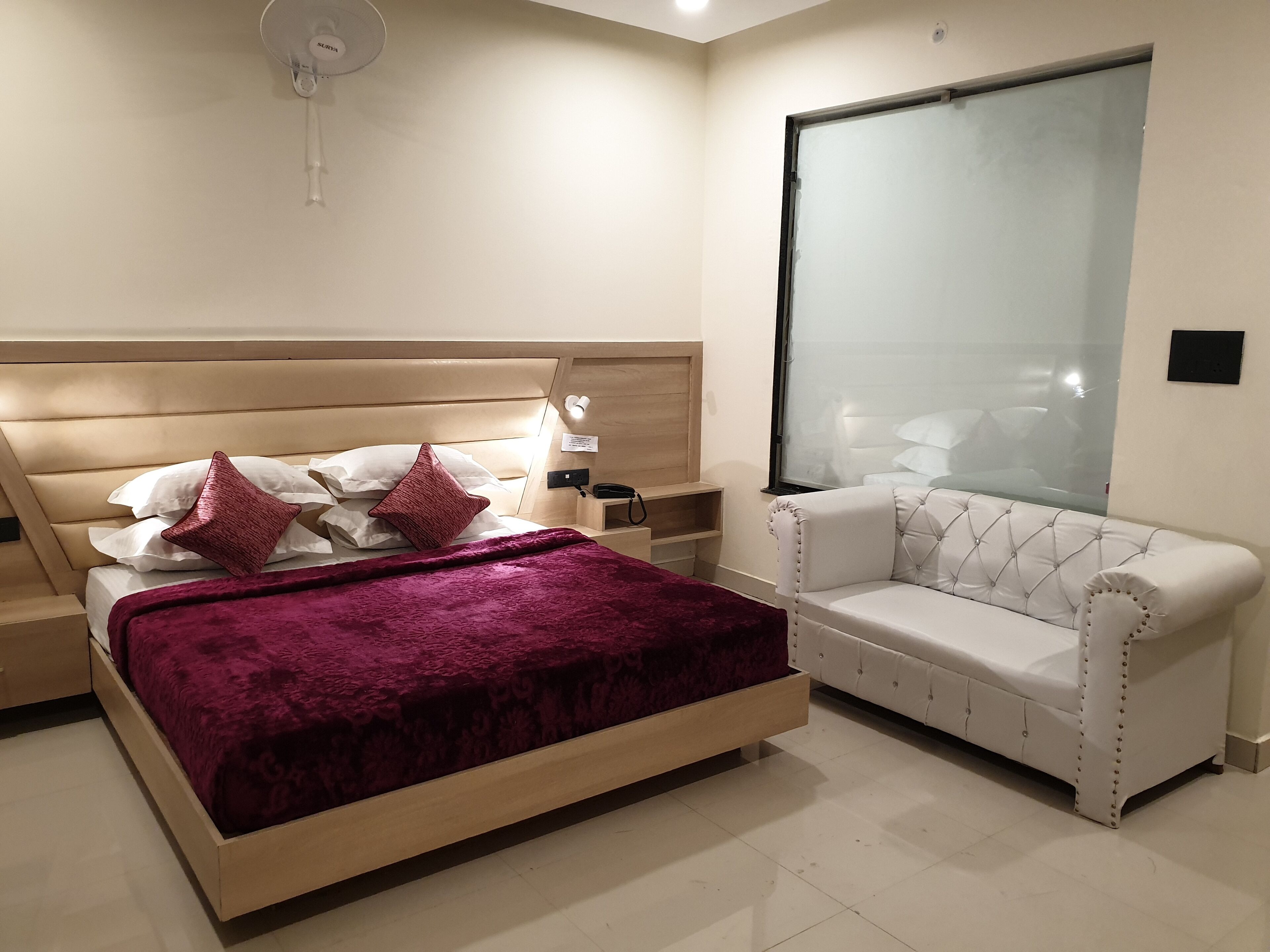 A bedroom with a bed, a nightstand, a bedside table, a chair, and a large window.