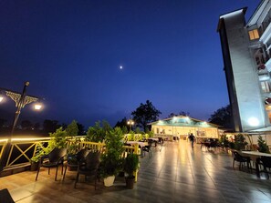 An outdoor patio area with tables and chairs, potted plants, and a building in the background. - Hotel Rajpur Heights (Dehradun)