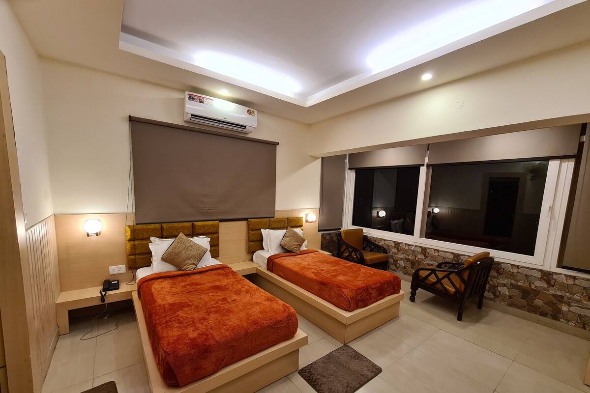 A hotel room with two beds, a desk, a chair, a window with a view, and an air conditioning unit.