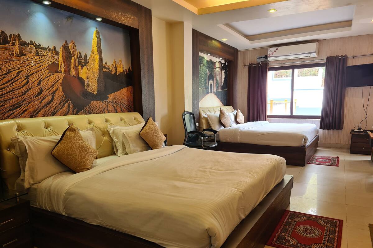 A hotel room with two beds, a large wall mural, a window with curtains, and an air conditioning unit.