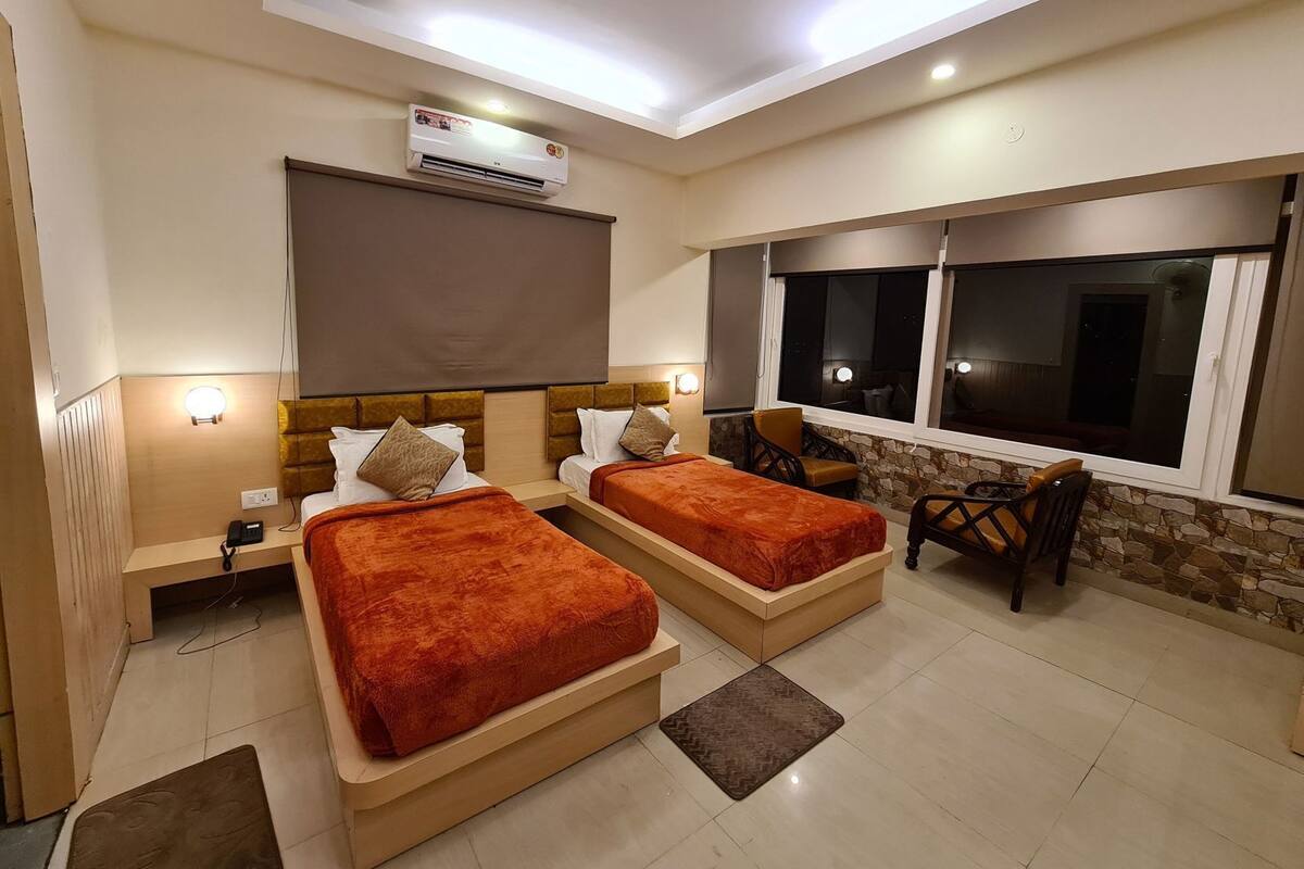 A hotel room with two beds, a desk, a chair, an air conditioning unit, and a window.