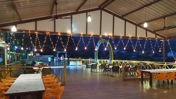 An outdoor dining area with tables and chairs, string lights overhead, and a view of the surrounding landscape. - Hotel Rajpur Heights (Dehradun)