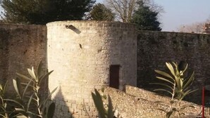 Una torre de piedra con una pequeña puerta, rodeada por un muro de piedra y árboles.