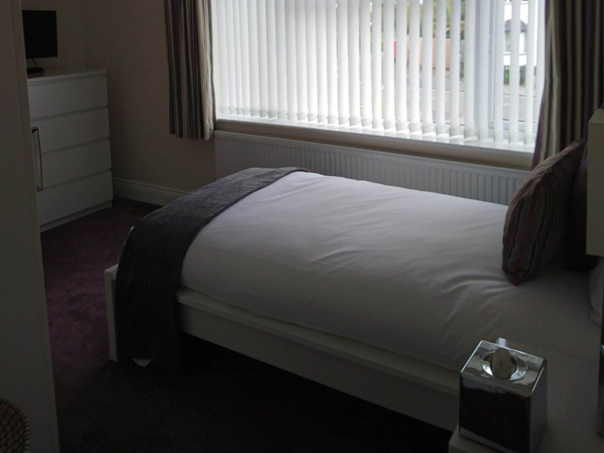 A bedroom with a bed, a dresser, a radiator, and a window with blinds.