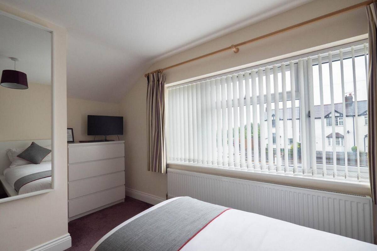 Une chambre d’hôtel avec un lit, une commode, une télévision et une fenêtre avec des stores.