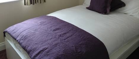 A single-bed room with a white headboard, a purple throw blanket, and a white pillow.