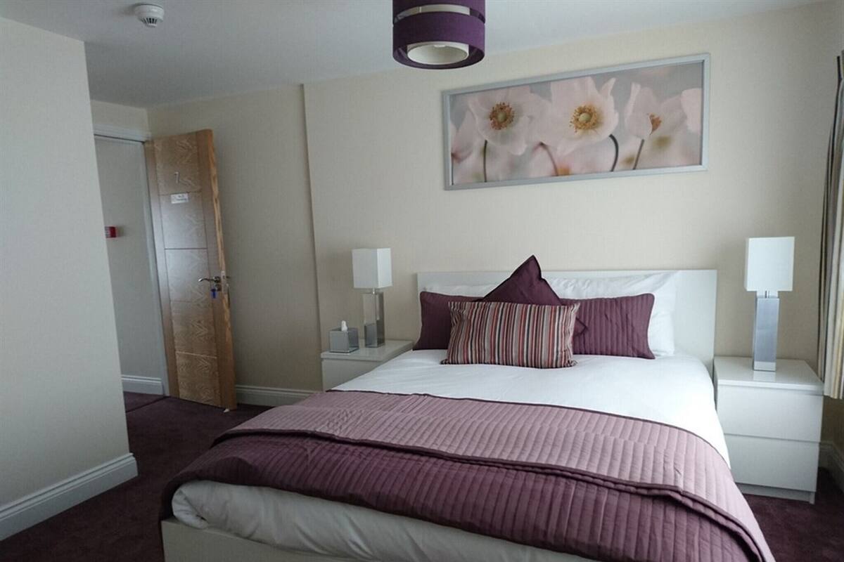 Une chambre d’hôtel avec un lit, des tables de chevet, un tableau et une porte.