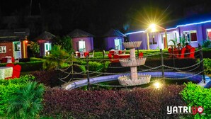 A nighttime view of a resort with a central fountain, surrounded by well-maintained gardens and small buildings with purple facades. - Suva Hotel (Birendranagar)