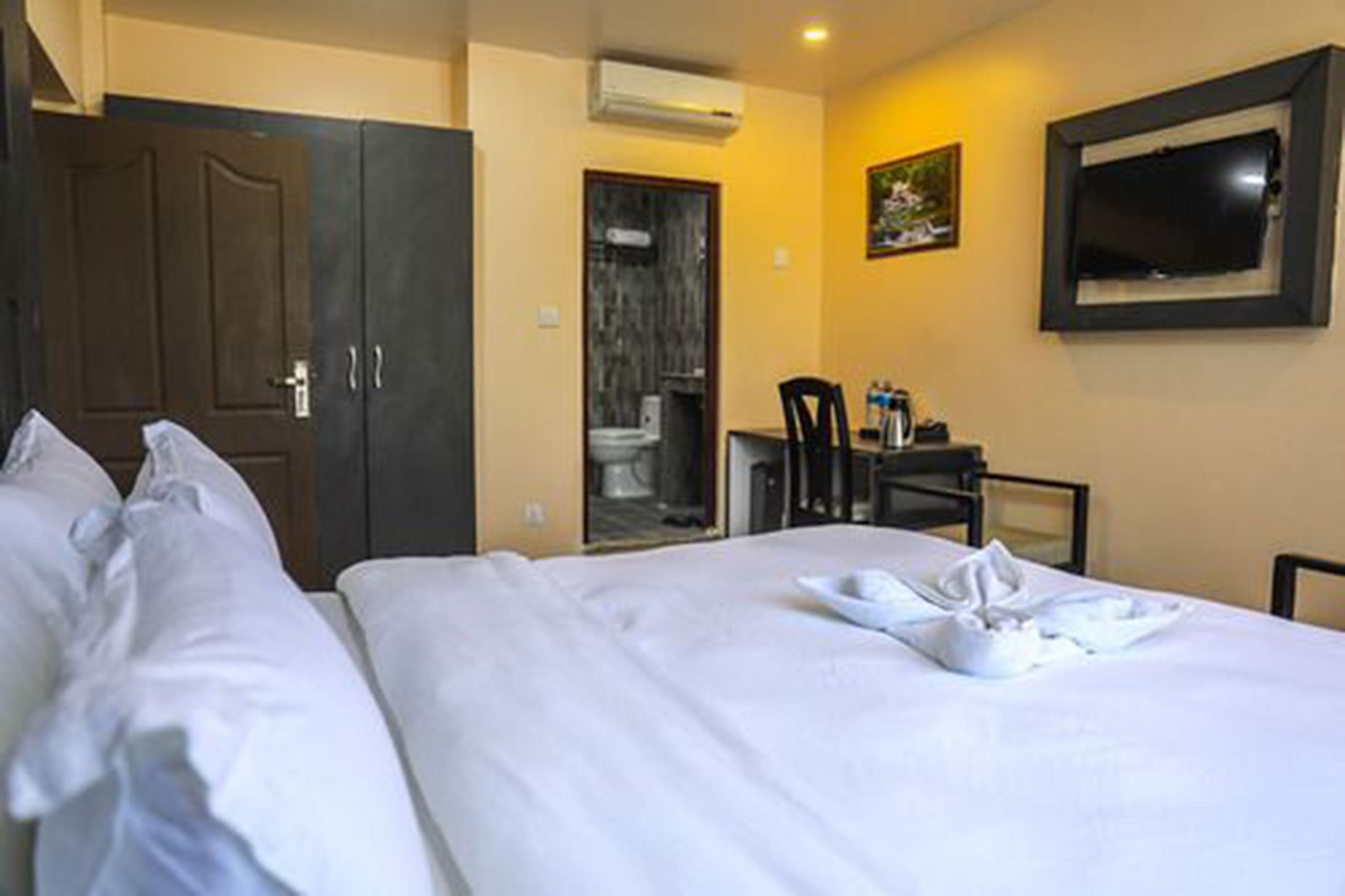 A hotel room with a bed, a desk with a chair, a television, and a door leading to a bathroom.