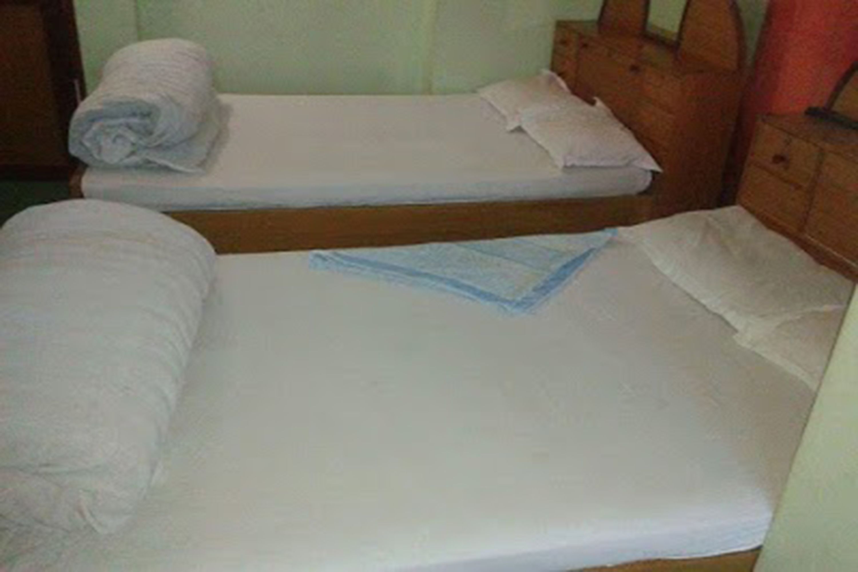 Une petite pièce simple, avec deux lits simples, chacun doté d’un matelas blanc et d’une serviette blanche enroulée.