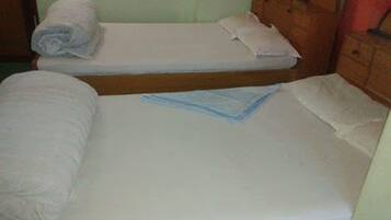 Une petite pièce simple, avec deux lits simples, chacun doté d’un matelas blanc et d’une serviette blanche enroulée.