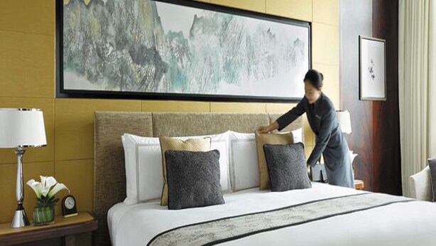 A hotel room with a large bed, a nightstand with a lamp and a clock, and a painting on the wall. - Suva Hotel (Birendranagar)