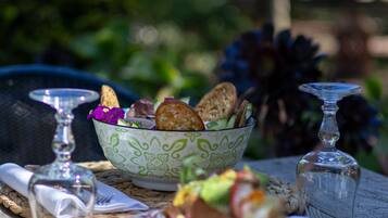 A table set with a bowl of salad, bread, and a glass of water, with a wicker chair and a glass in the background.