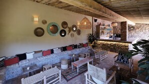 A cozy lounge area with a sofa, chairs, and a bar area with stone walls and wooden beams. - Pozzo di Mastri (Figari)