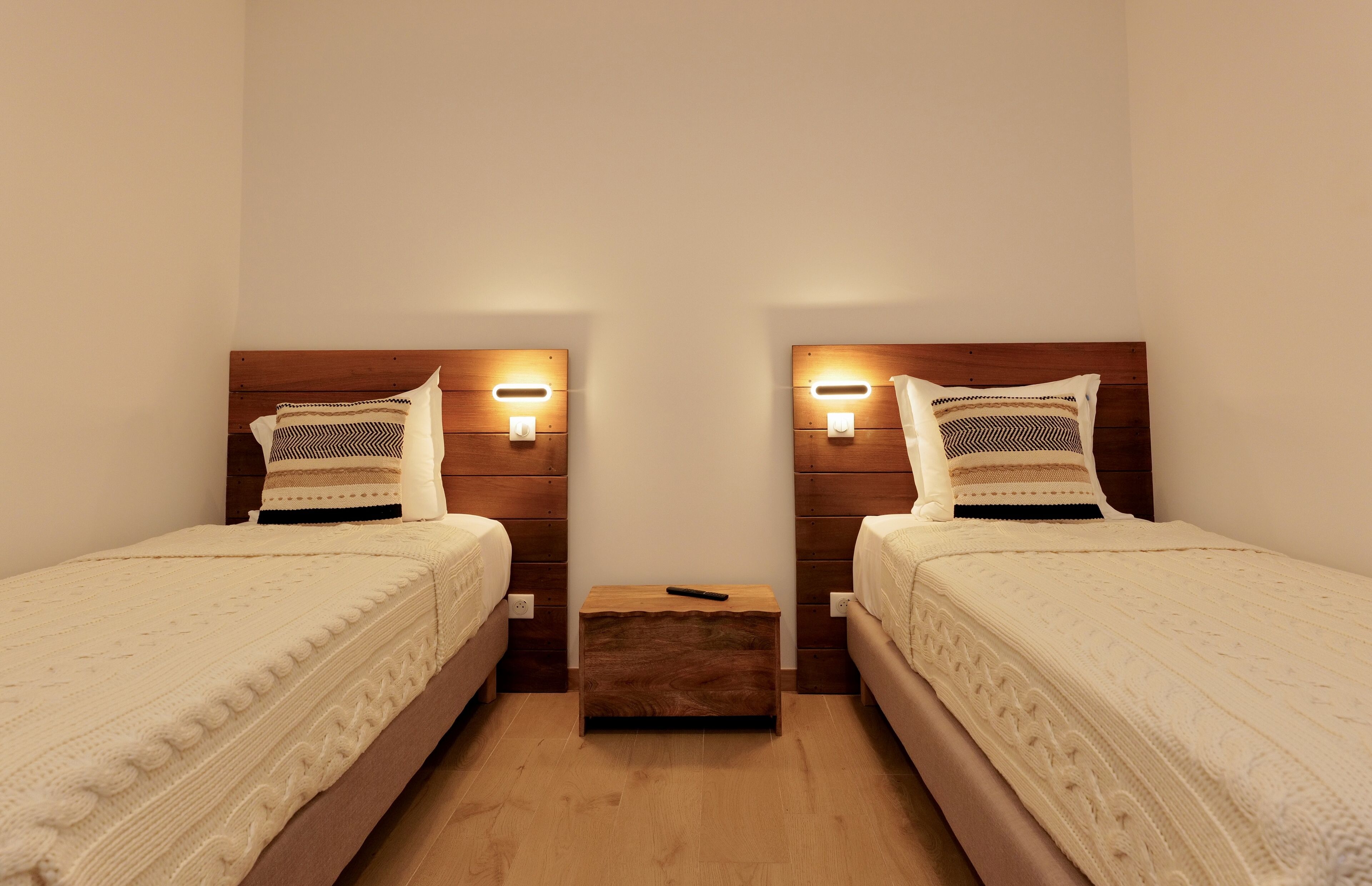 Une chambre double avec deux lits, chacun doté d’une tête de lit en bois et d’une table de chevet.