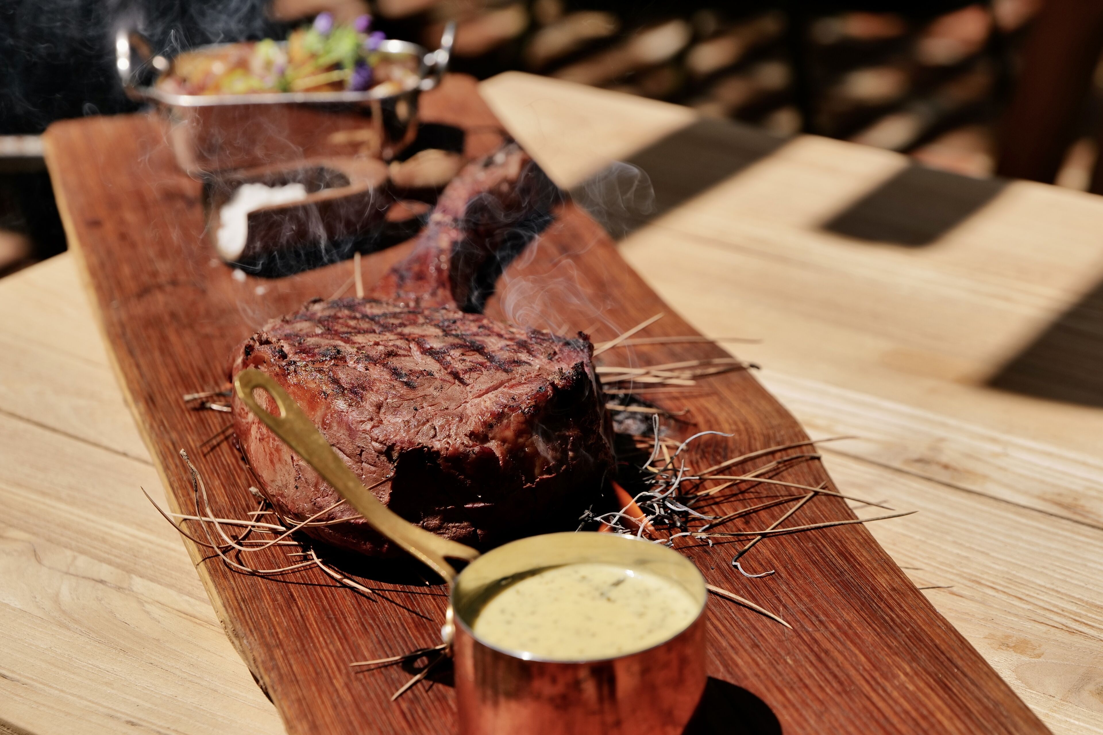 Un grand steak grillé, servi sur une planche en bois avec une sauce pour tremper et une fourchette.