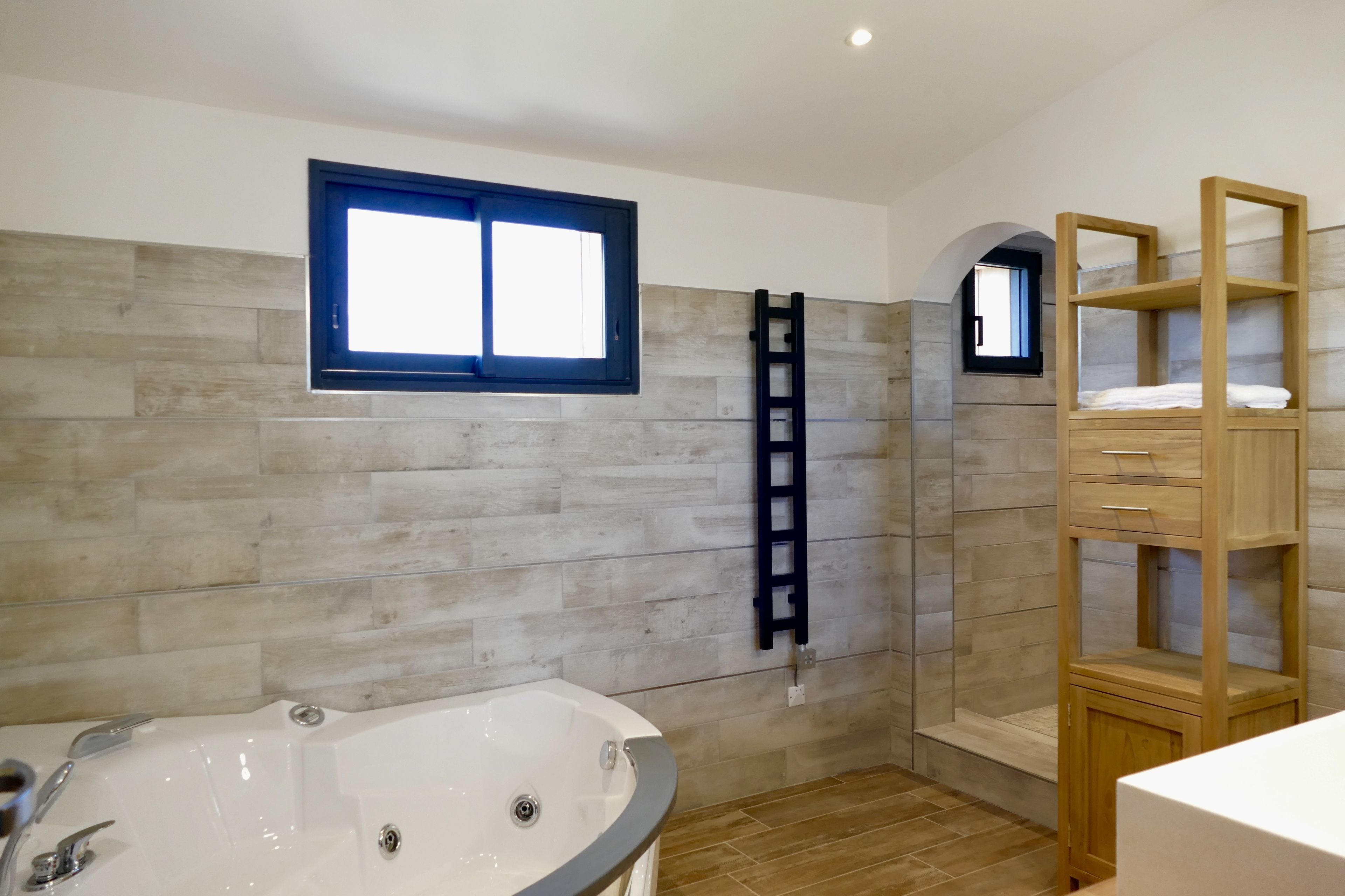 Une salle de bain moderne avec une baignoire, des étagères en bois et une fenêtre.