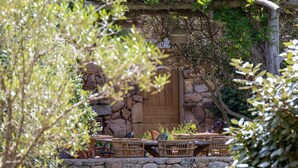A stone wall with a wooden door, wicker furniture, and a stone bench. - Pozzo di Mastri (Figari)