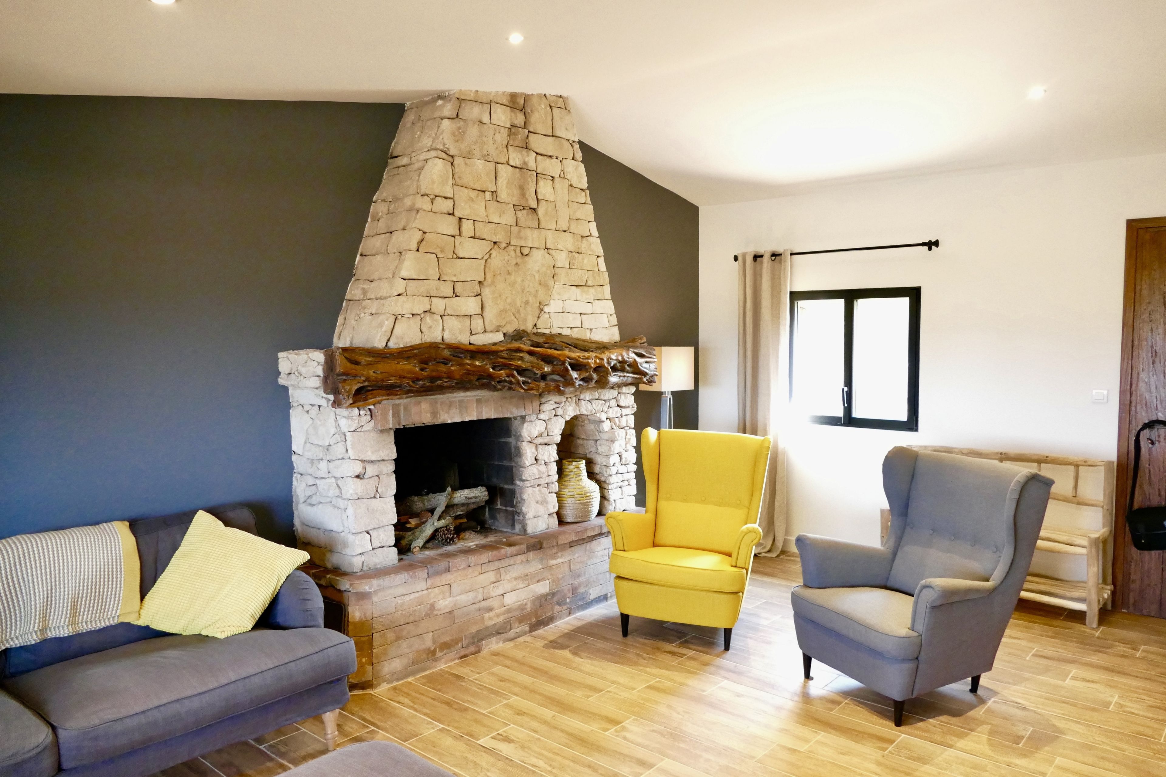 A living room with a stone fireplace, two armchairs, a sofa, and a wooden floor.