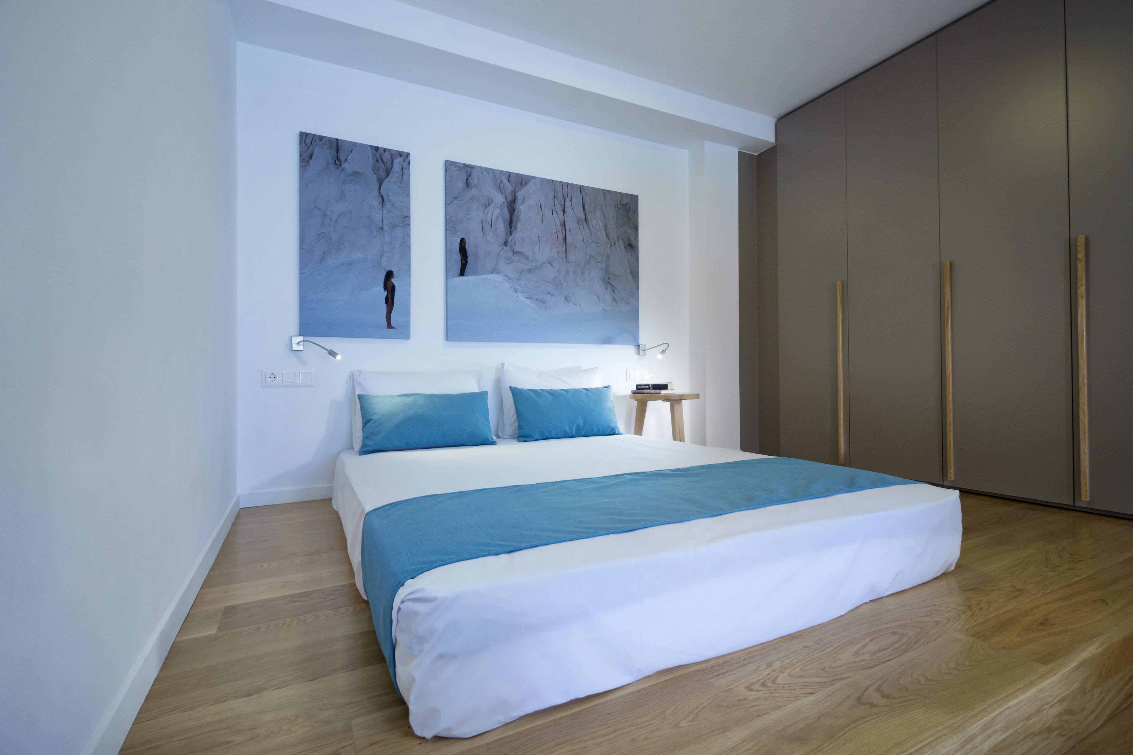 Quarto moderno com uma cama grande, duas pinturas penduradas na parede, uma mesa de cabeceira e um guarda-roupa.