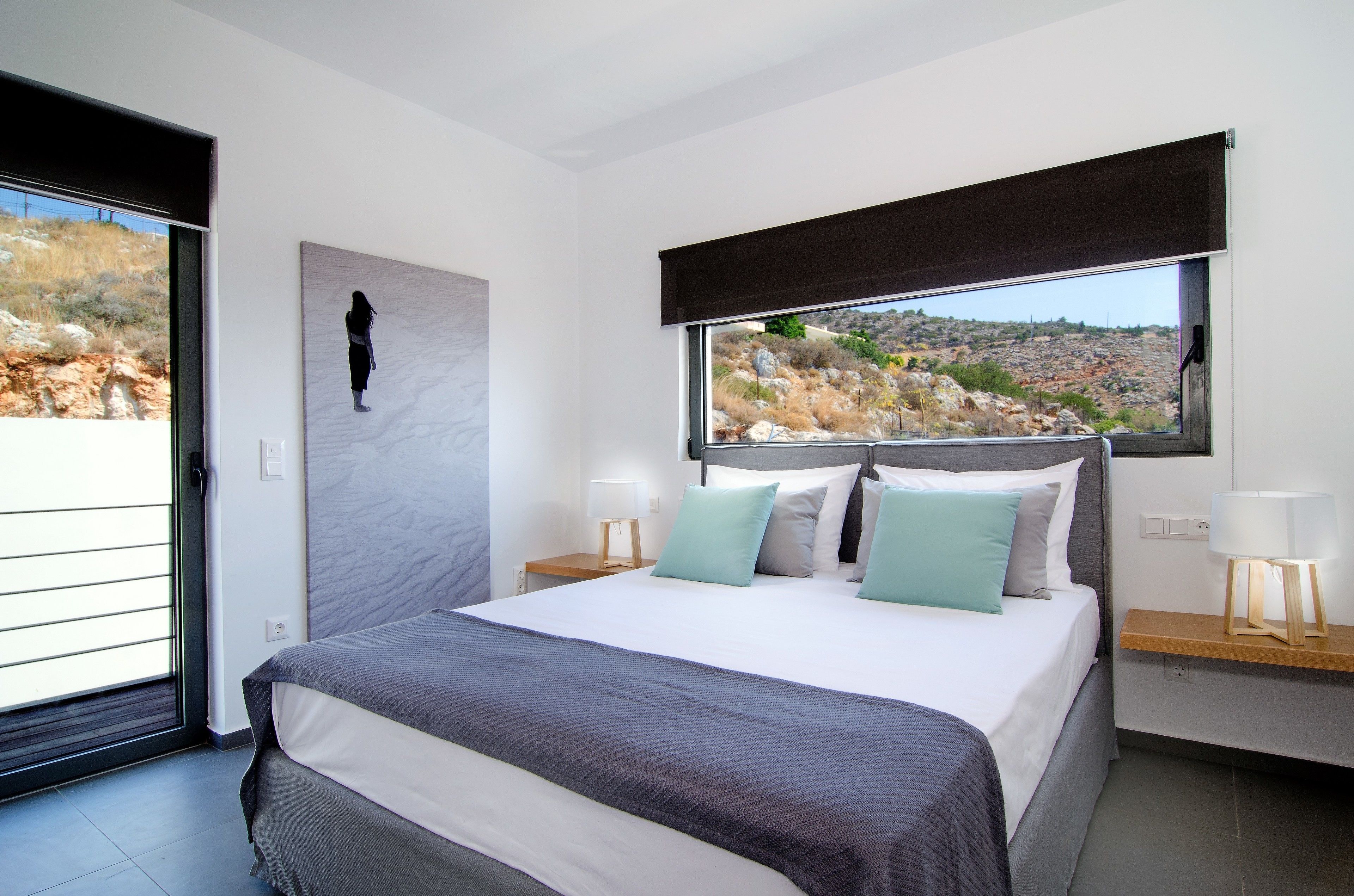 Ein modernes Schlafzimmer mit einem großen Bett, Blick auf eine felsige Landschaft und einer Schiebetür.