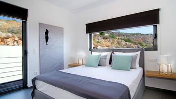 Ein modernes Schlafzimmer mit einem großen Bett, Blick auf eine felsige Landschaft und einer Schiebetür.