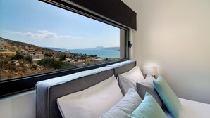 Een hotelkamer met een groot raam met uitzicht op een kustplaatsje en de zee.