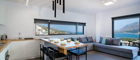 A modern kitchen with a dining area, large windows, and a view of the sea.