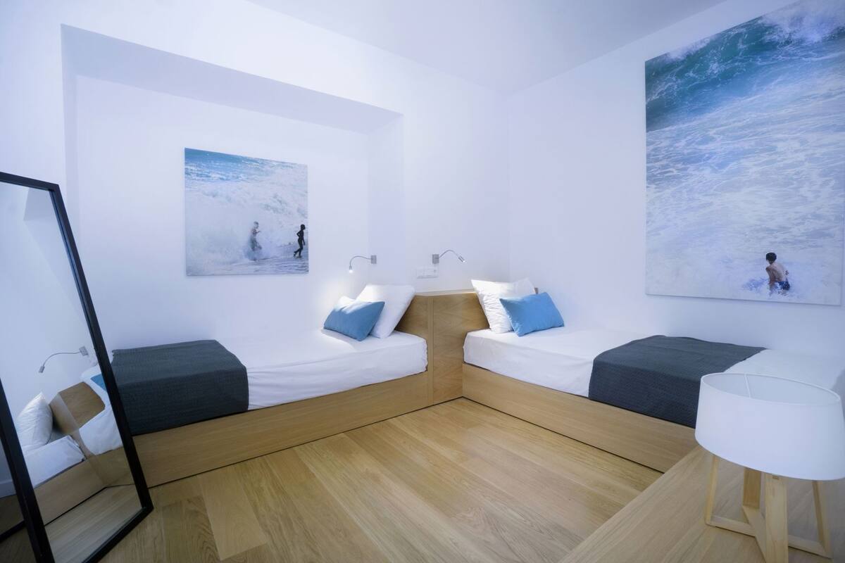 Een moderne, minimalistische kamer met twee bedden, een grote spiegel en kunstwerken met afbeeldingen van zeegezichten.