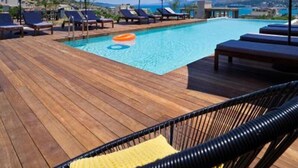 Een houten terras met een zwembad, ligbedden en parasols.