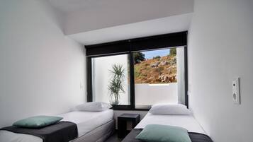 Un dormitorio moderno con dos camas individuales, una mesita de noche pequeña y un ventanal con vistas a un paisaje rocoso.