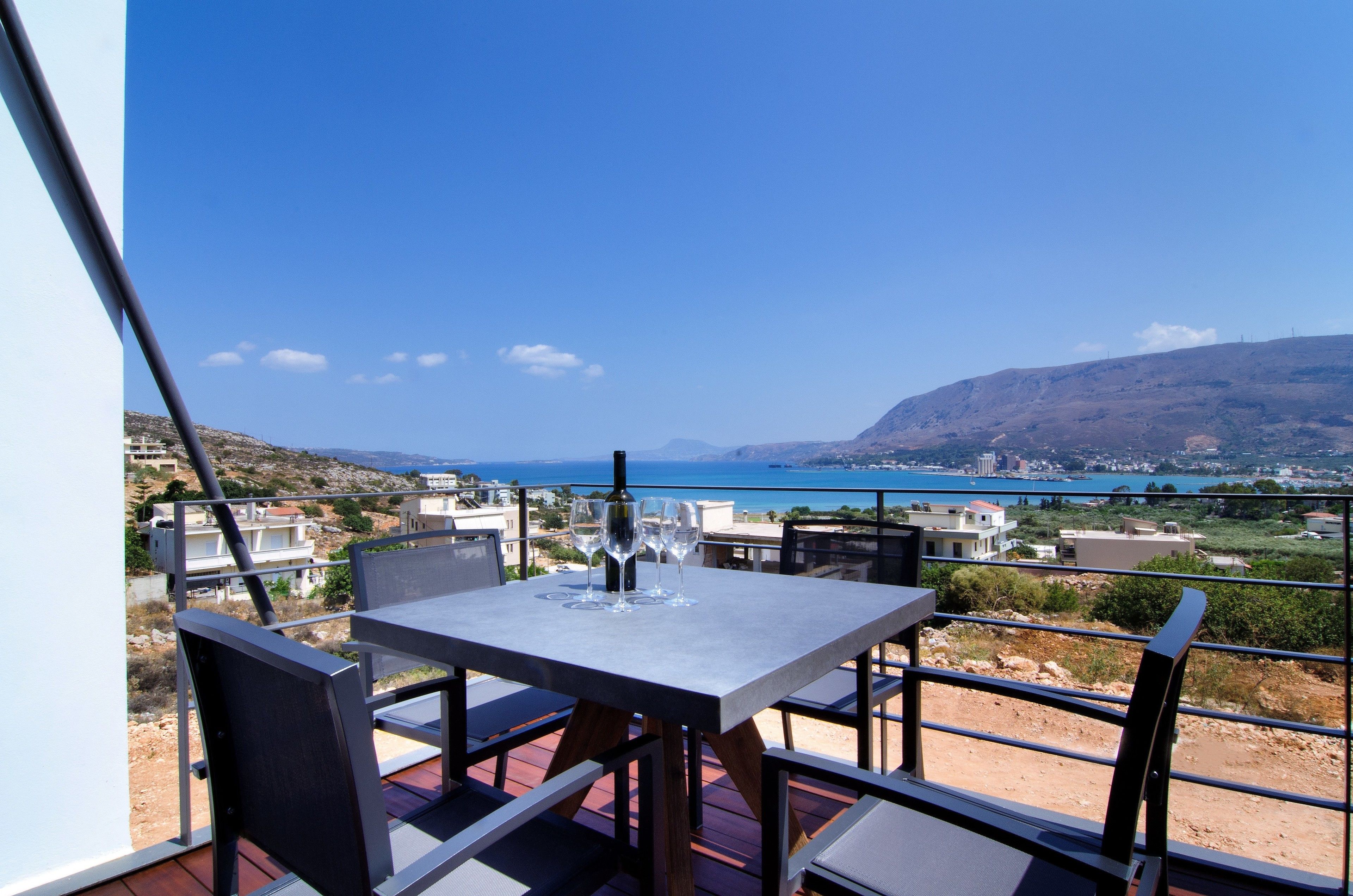 A table with chairs on a balcony overlooking a scenic view of a coastal town and the sea.