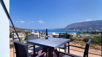 A table with chairs on a balcony overlooking a scenic view of a coastal town and the sea.