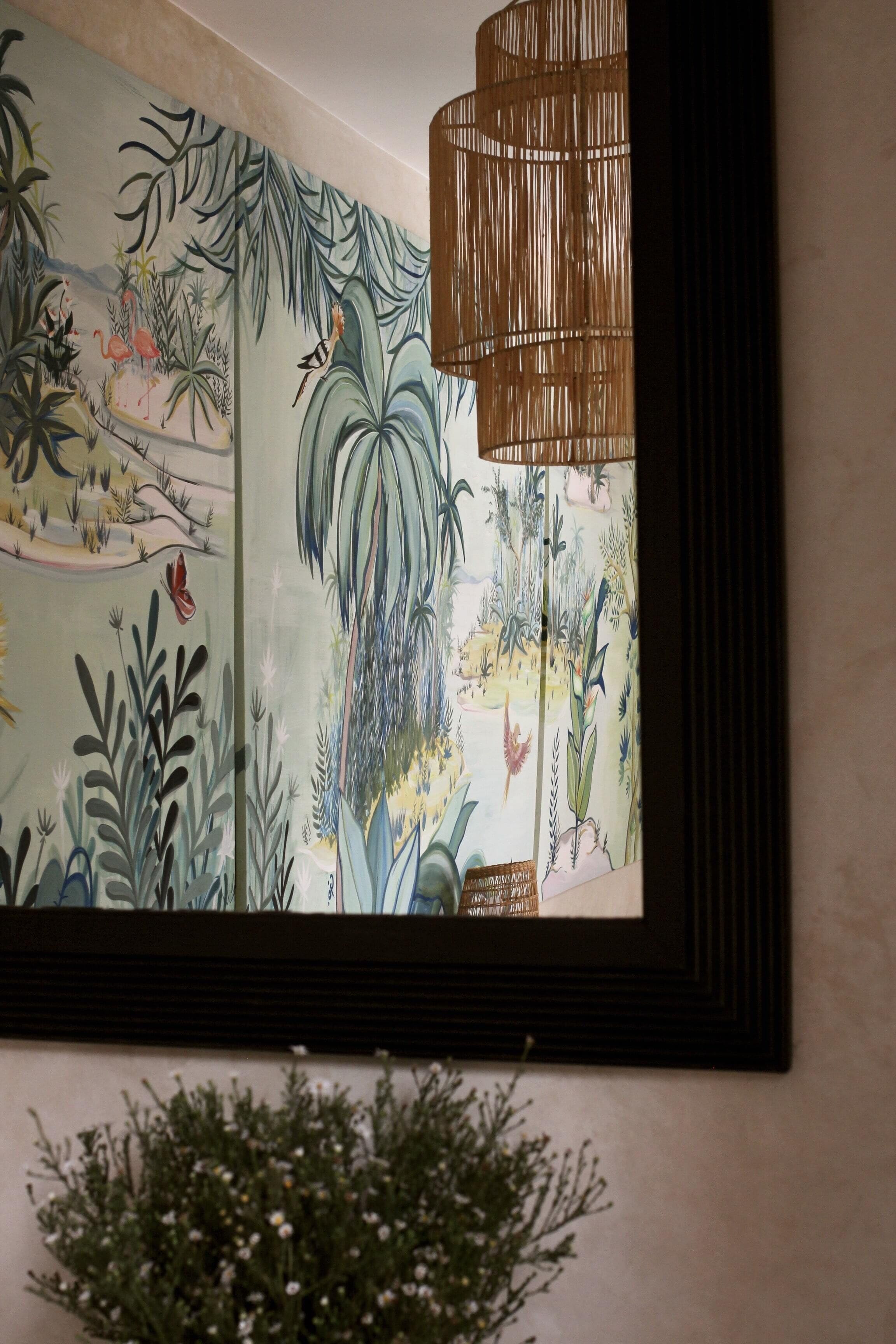 A wall with a mural of tropical plants and a hanging lamp.