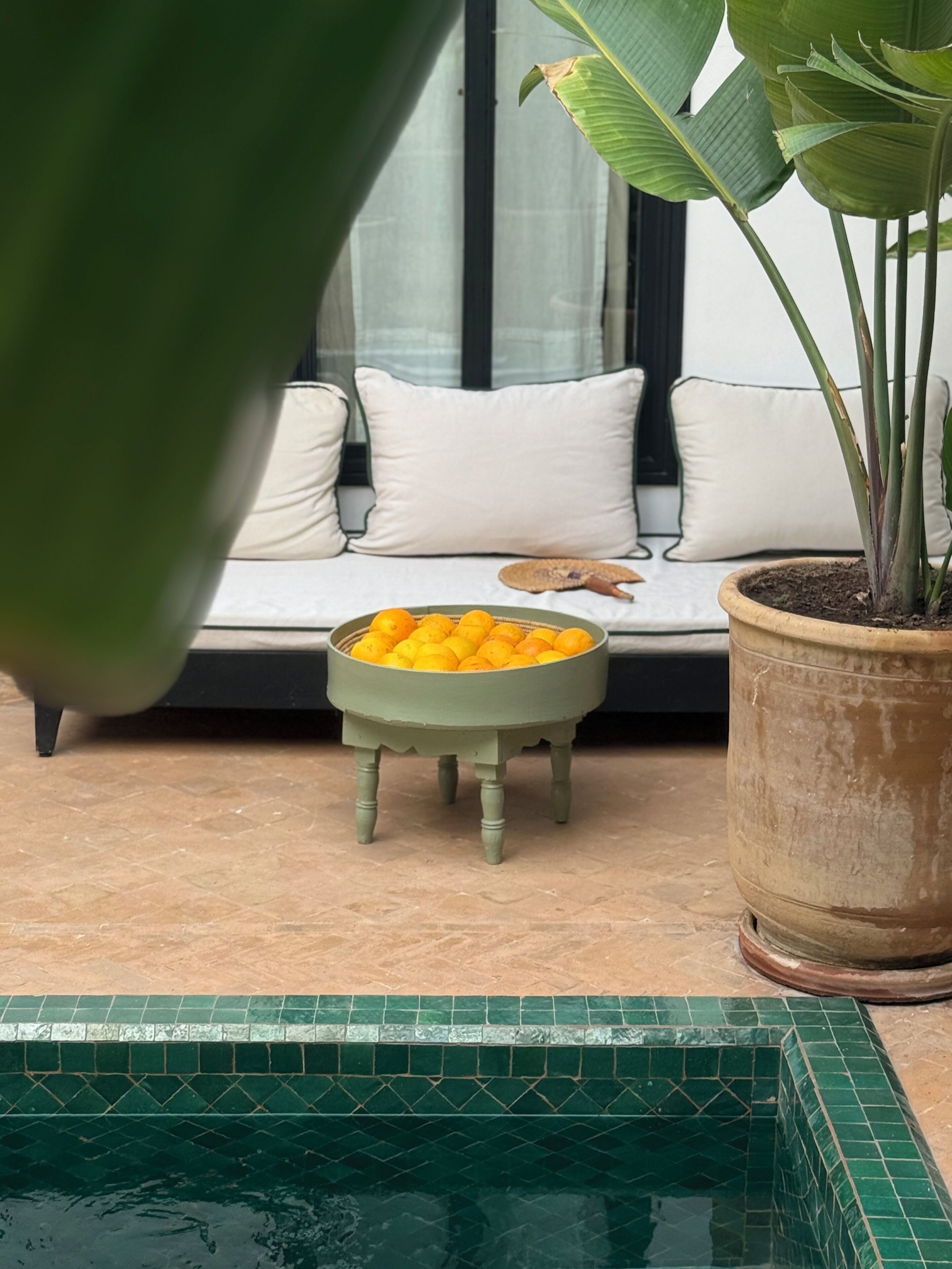 A poolside area with a white sofa, a small round table with oranges, and a potted plant.