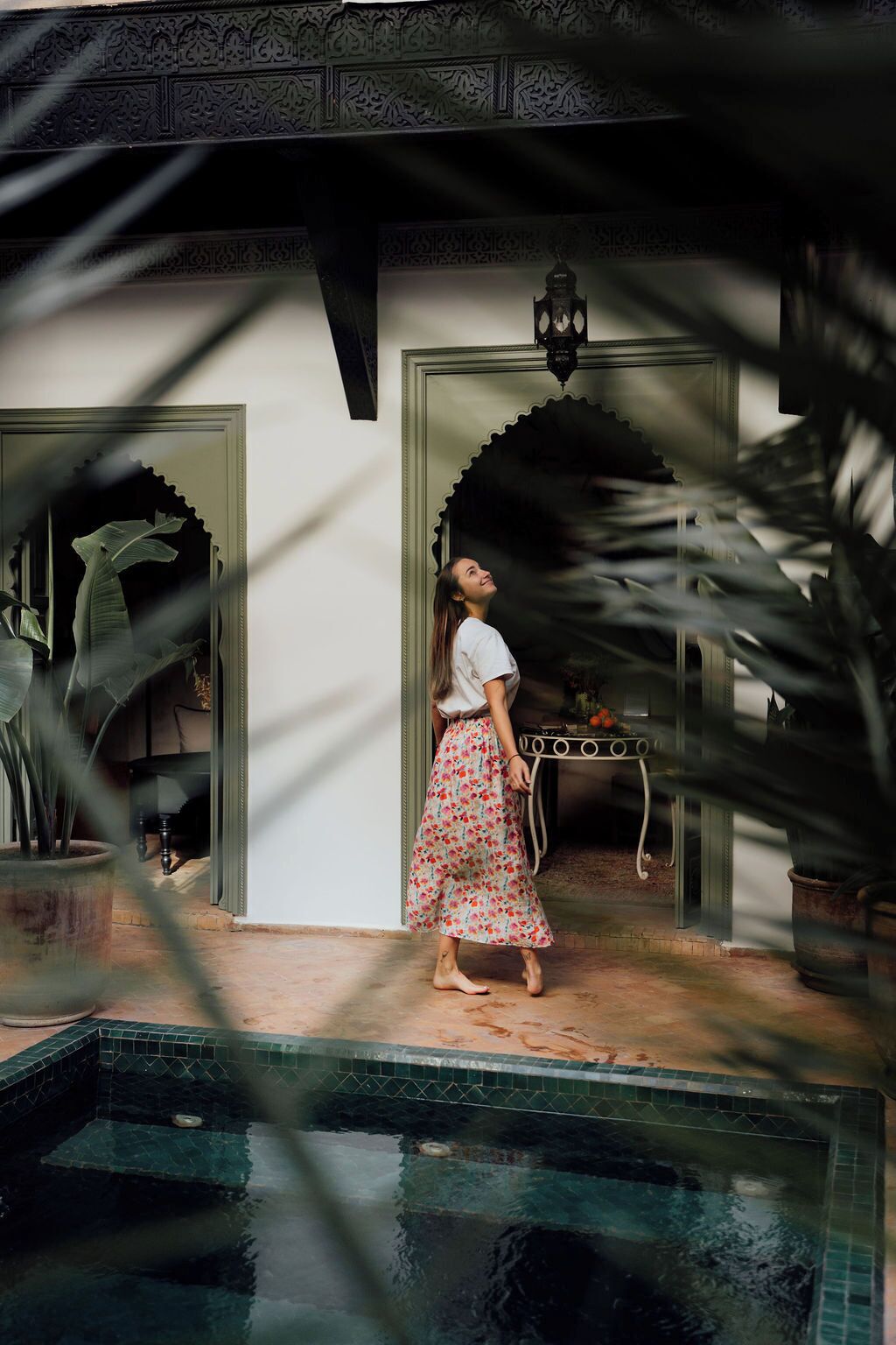 A person standing by a pool with a traditional architectural entrance and a decorative lantern.