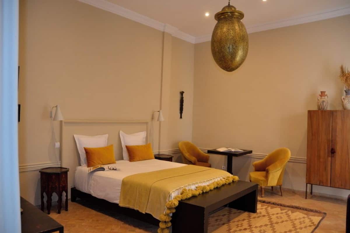 A bedroom with a bed, bedside tables, a desk, two chairs, a hanging lamp, and a wardrobe.
