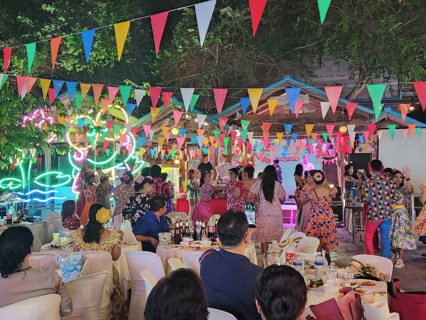 Un evento festivo al aire libre con llamativas banderas triangulares, luces de neón y una multitud de personas.