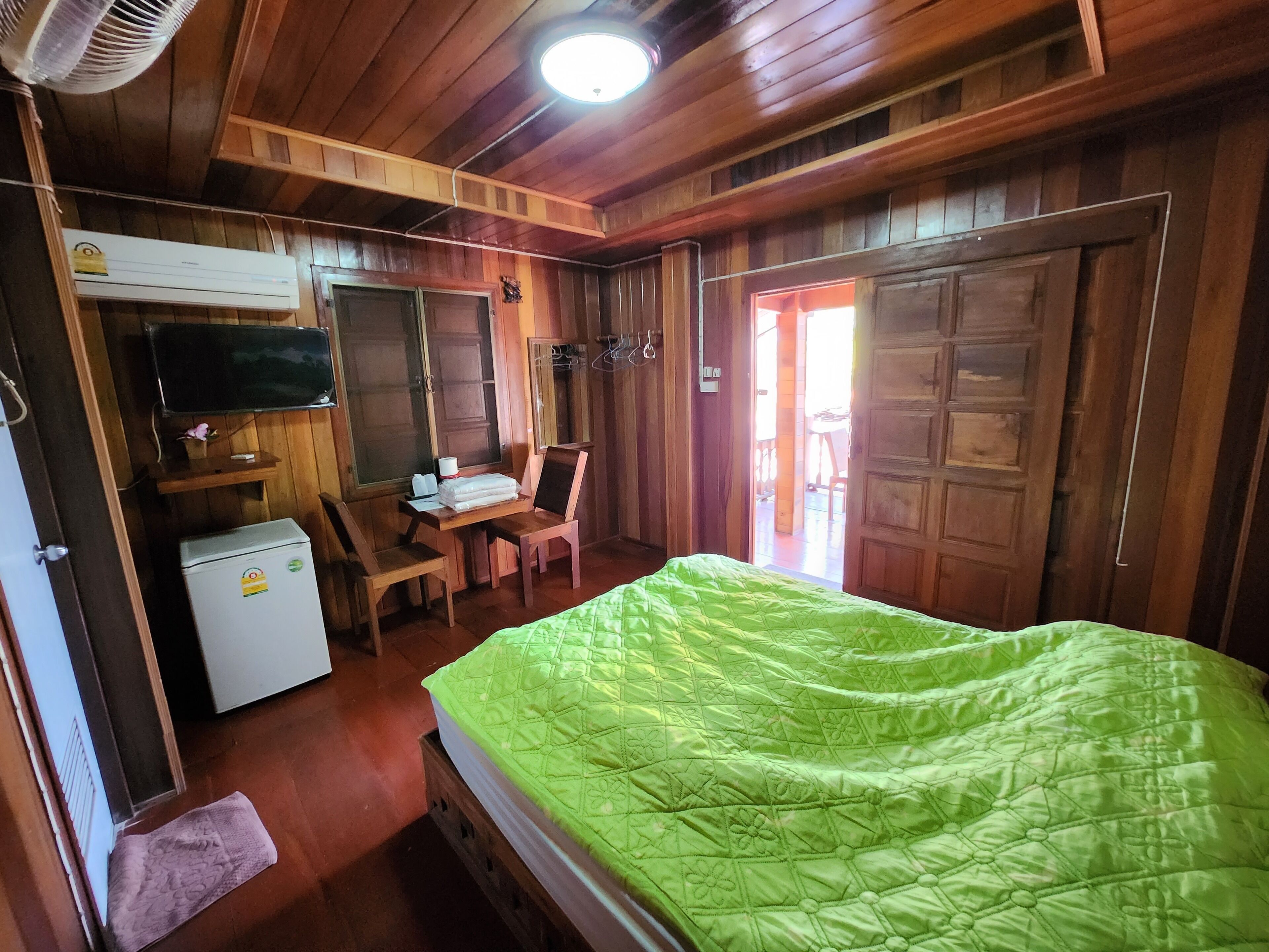 Ein Zimmer mit Holzboden, einem Bett, einem Schreibtisch, einem Stuhl und einem Fernseher.