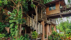 A rustic wooden house with a balcony, surrounded by lush greenery and potted plants. - Klong Suan Plu Resort (Ayutthaya)