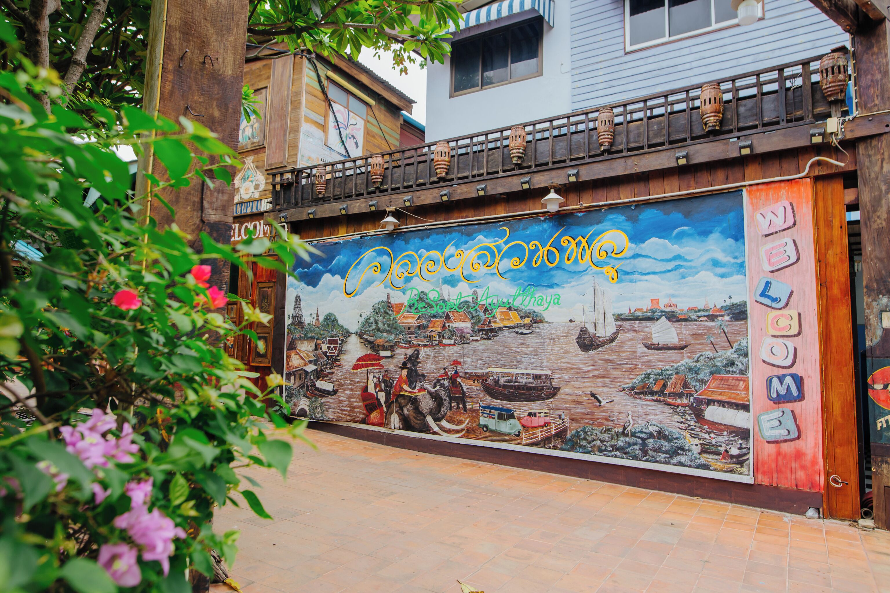 A mural with a traditional scene, a wooden balcony with hanging lanterns, and a sign that reads "WELCOME".
