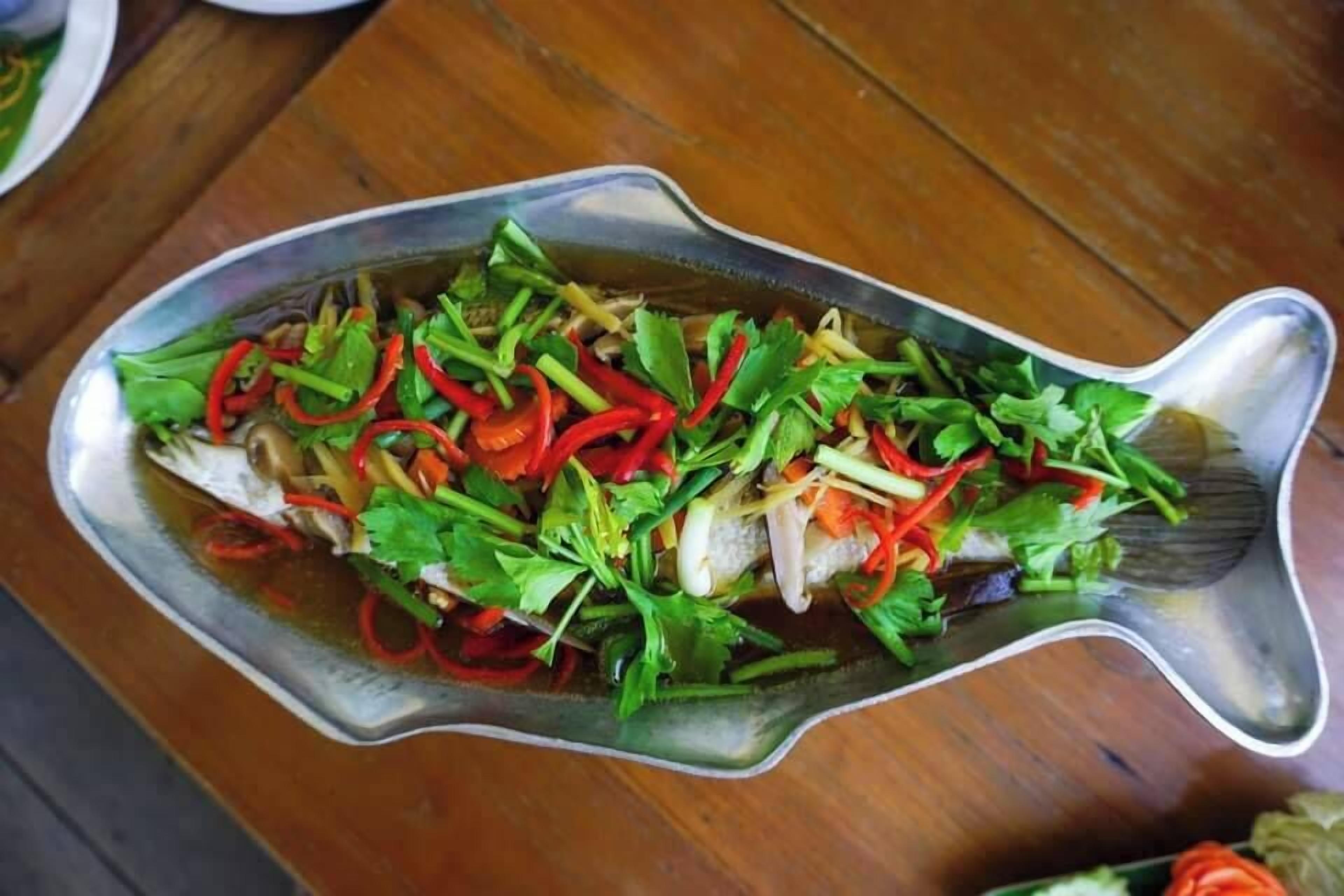 Un plato con forma de pez, con un filete de pescado y verduras sobre una mesa de madera.