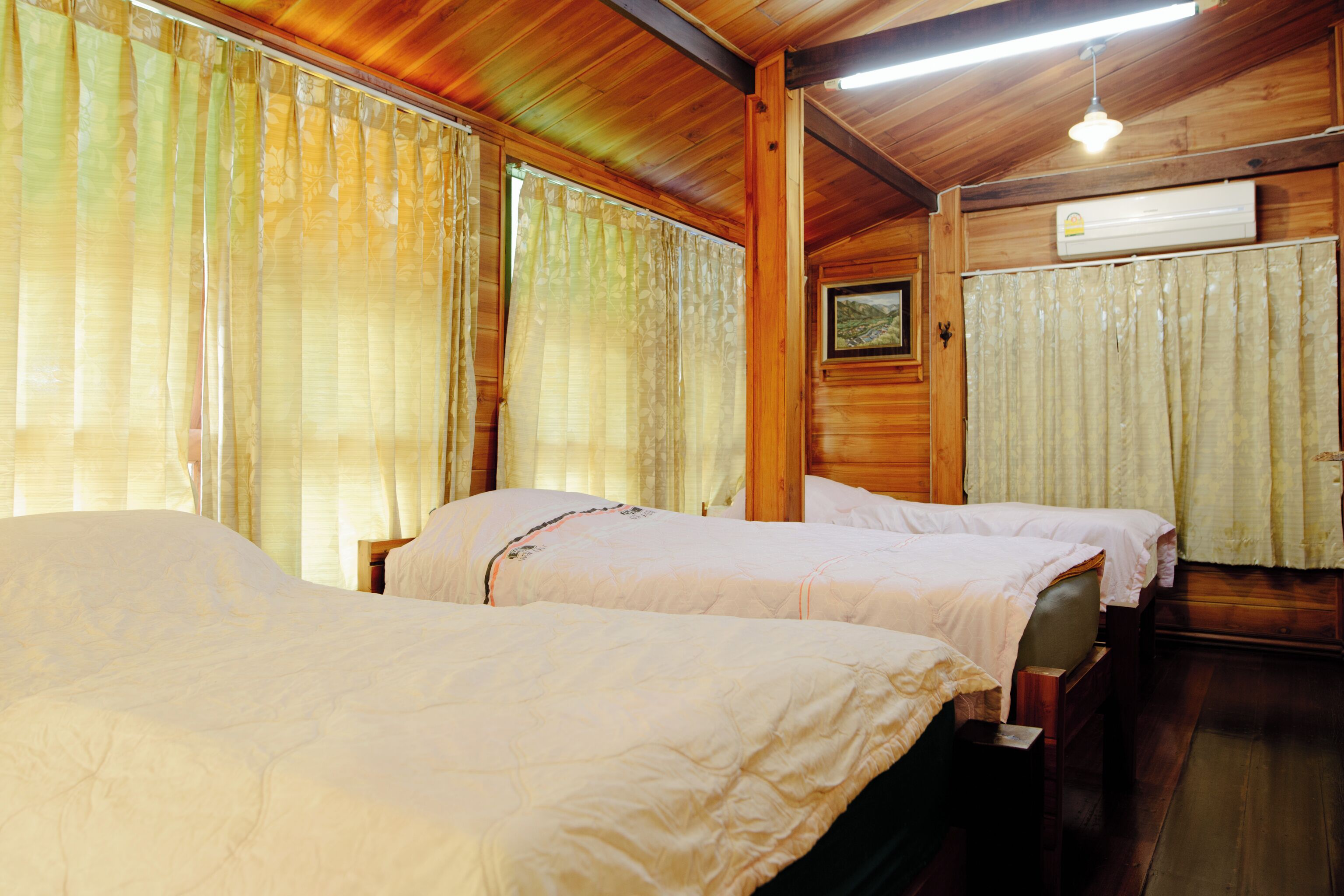 A room with two beds, wooden walls, and an air conditioning unit.