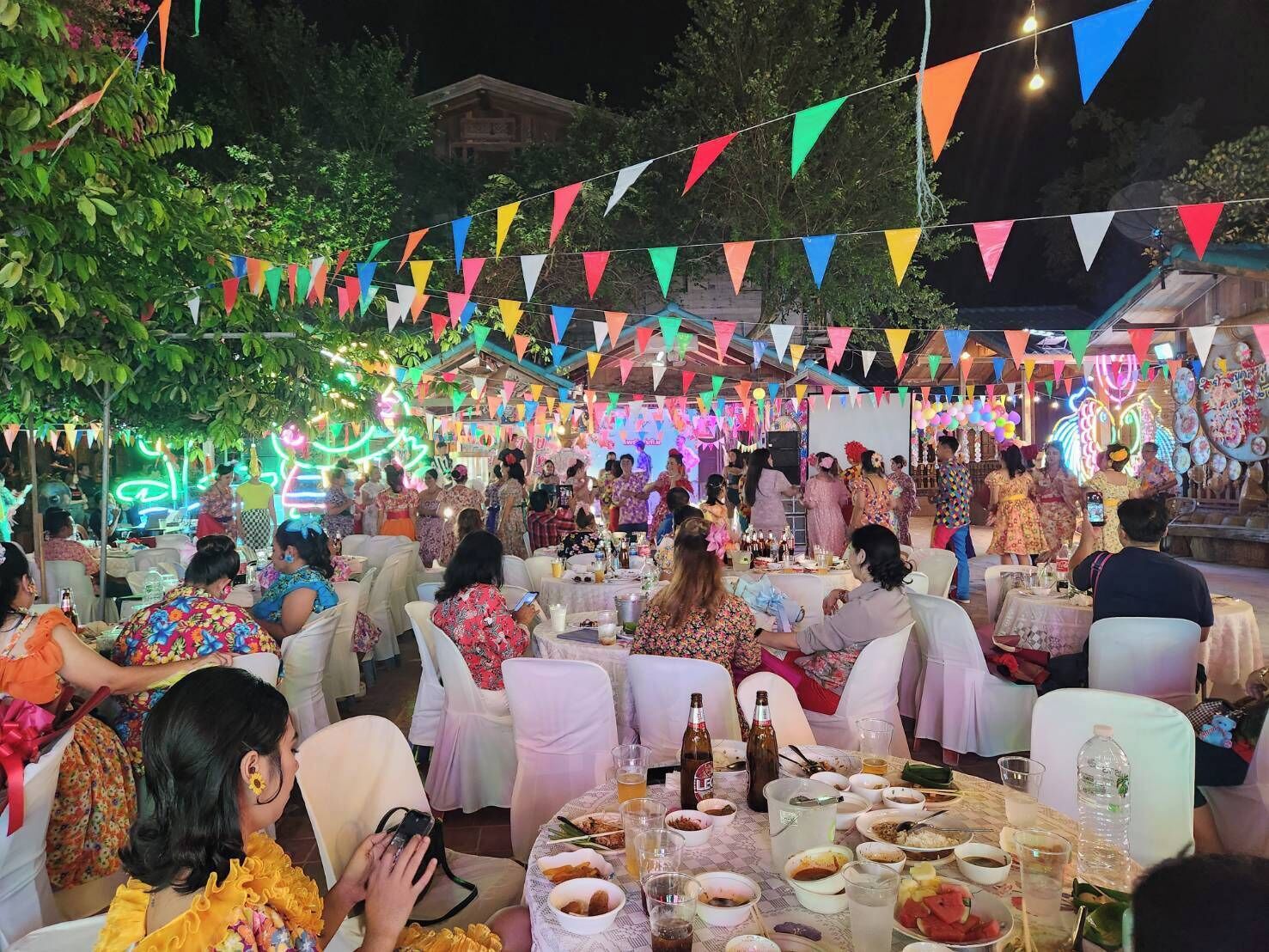 Evento ao ar livre com mesas montadas para refeições, rodeado por convidados.