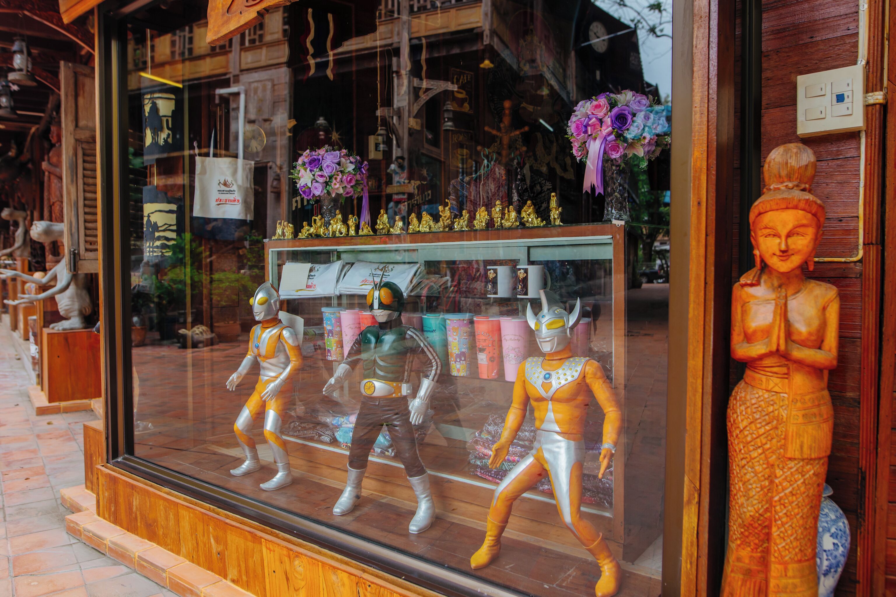 A storefront with mannequins in traditional attire, a Buddha statue, and various items on display.