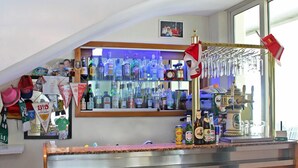A bar area with a wooden counter, shelves with bottles, and a window with natural light. - Hotel Royal (Misano Adriatico)